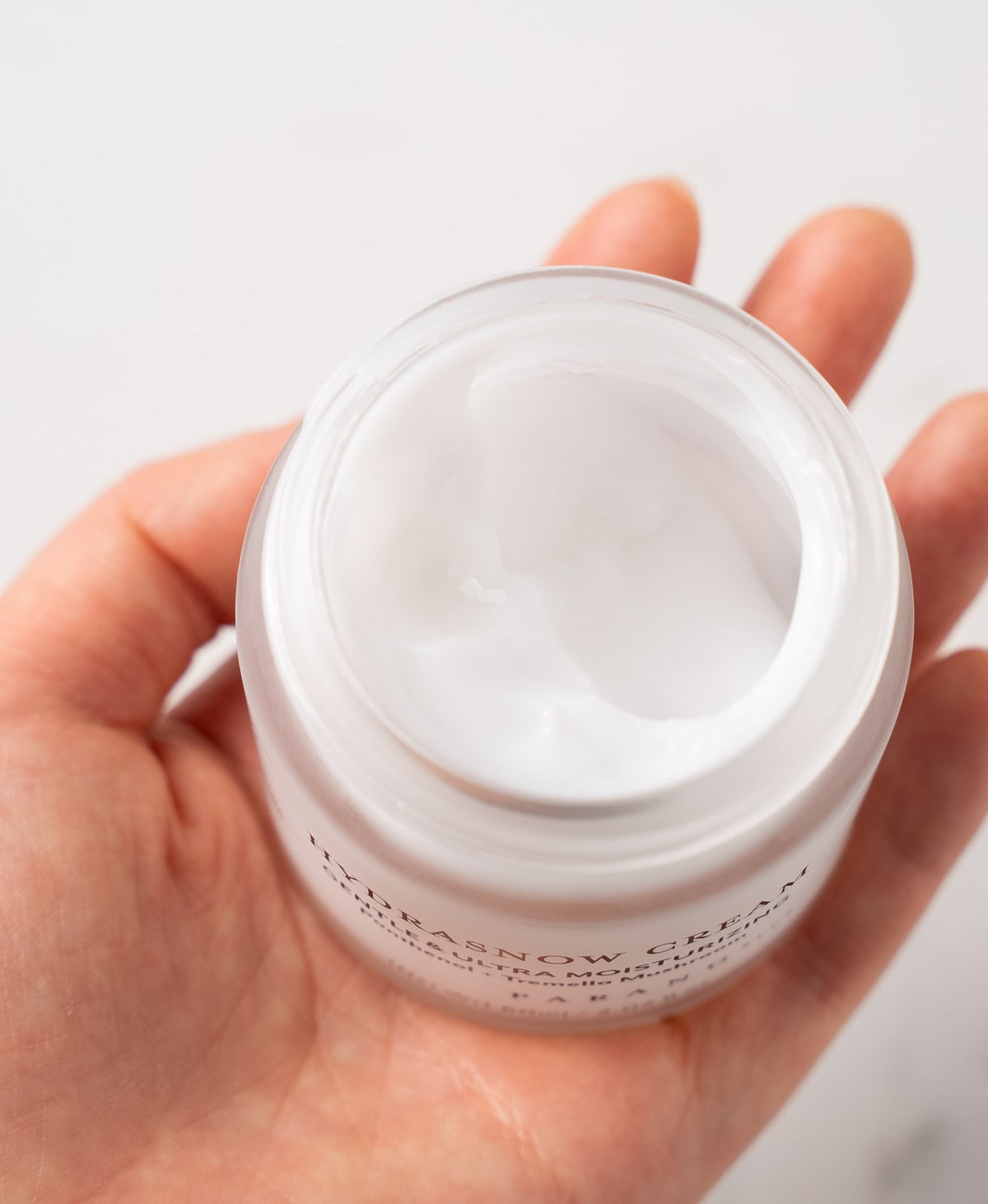 The open Hydrasnow Cream jar held in a hand
